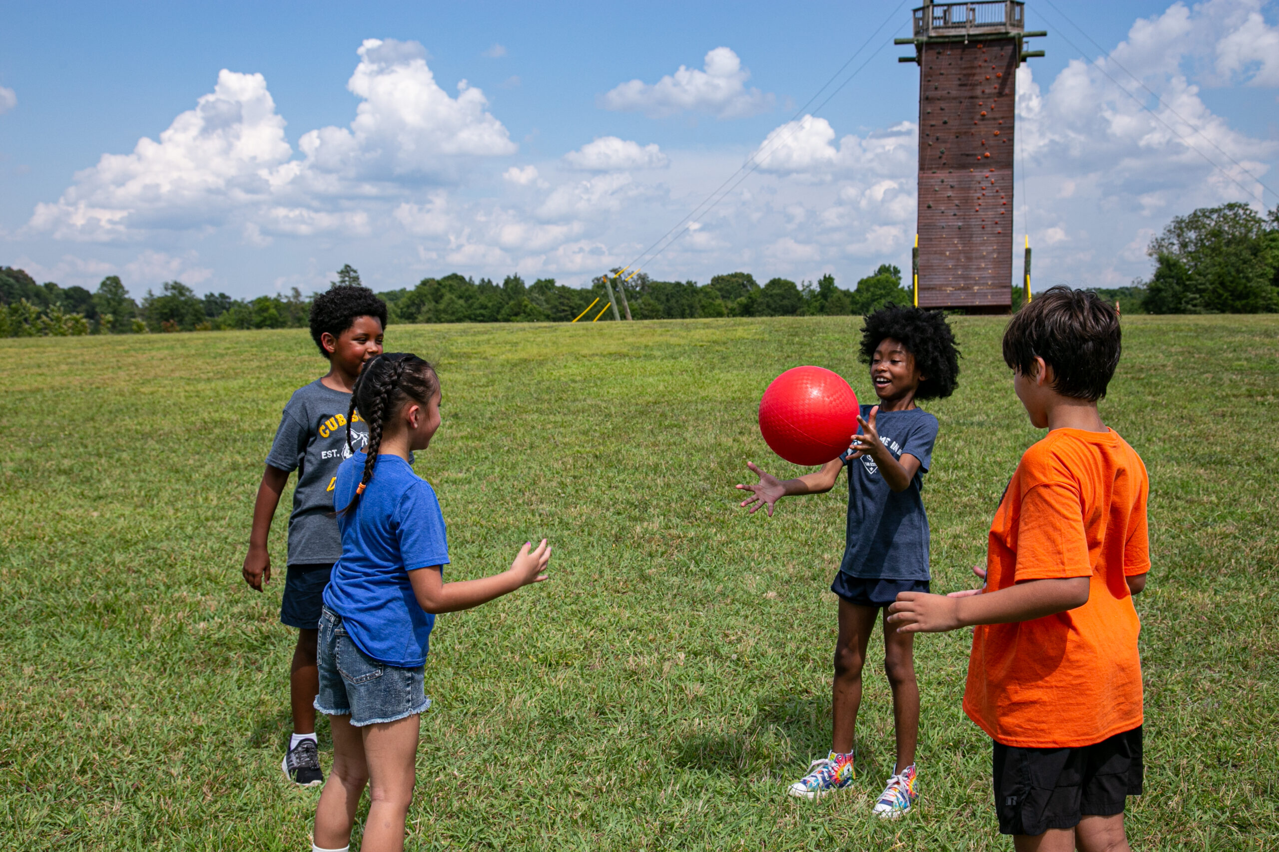 Playing catch with red ball in a field; climbing tower in background; park